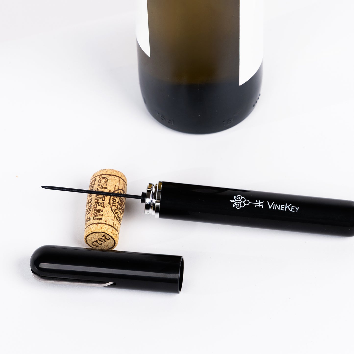 Lifestyle image of the VineKey black air pump wine opener pen next to a bottle and cork